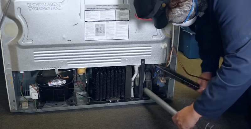A person repairs a refrigerator compressor and coils, focusing on appliance repair in Pensacola.