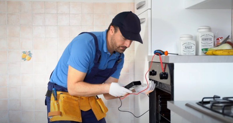 An appliance repair technician in Pensacola checks an oven with a multimeter.