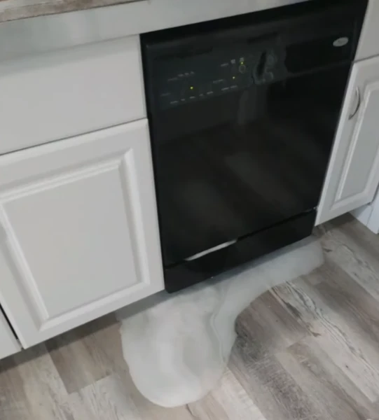 Dishwasher overflowing with foam onto kitchen floor, showing leak and malfunction.