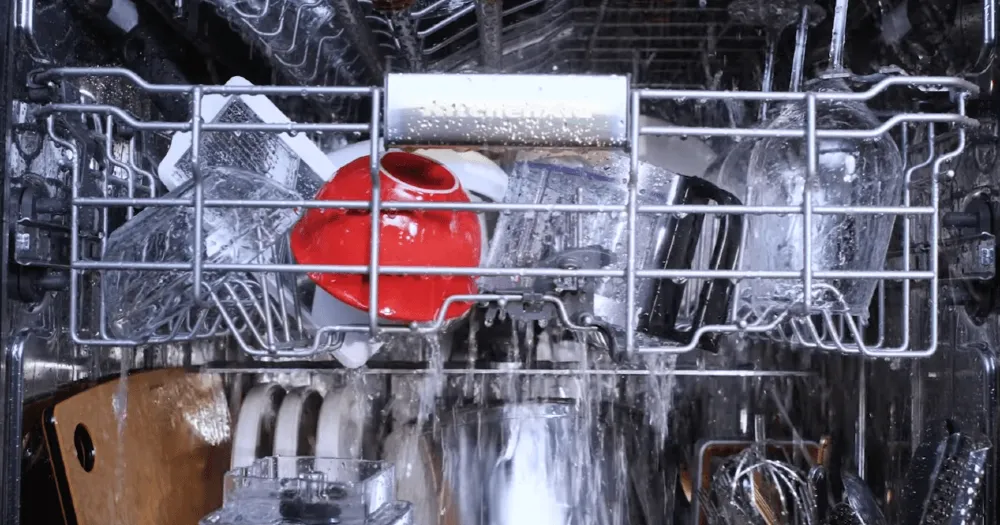 Red mug in running dishwasher with water spray showing not drying dishes issue.