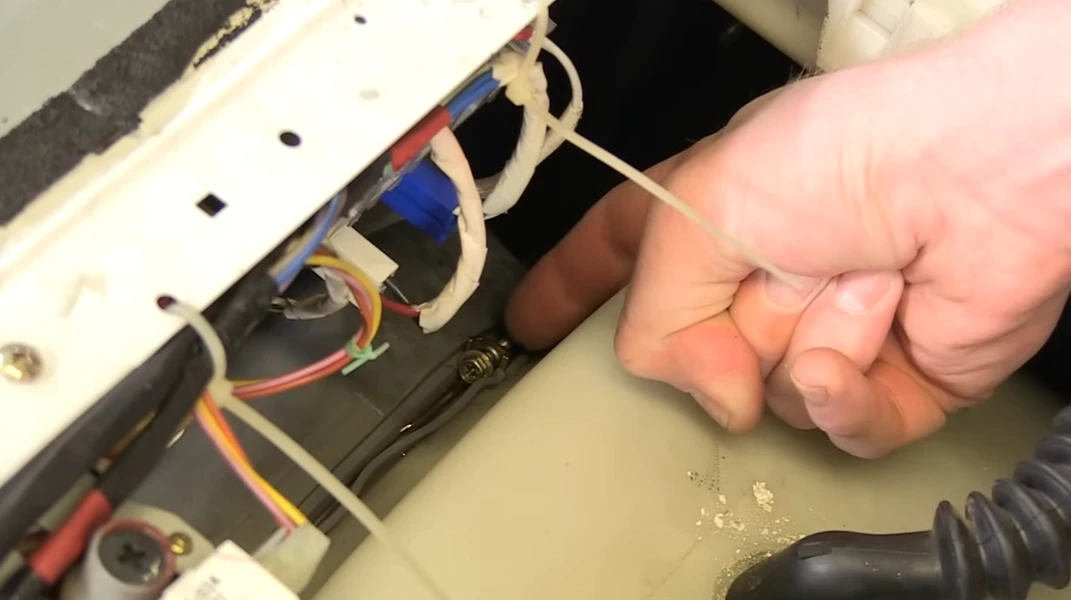 Hand gripping metal appliance part amid colorful wires during repair