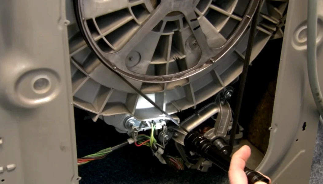 Hand shining flashlight on open washer back panel showing drum and motor wires