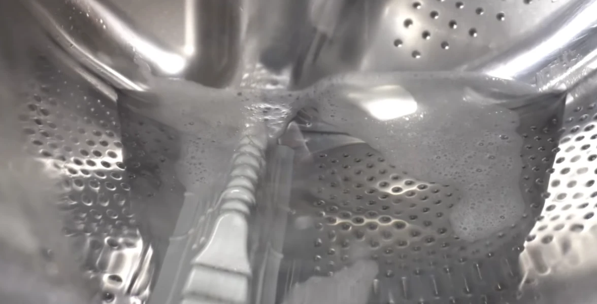 Soapy water and bubbles inside shiny silver washing machine drum